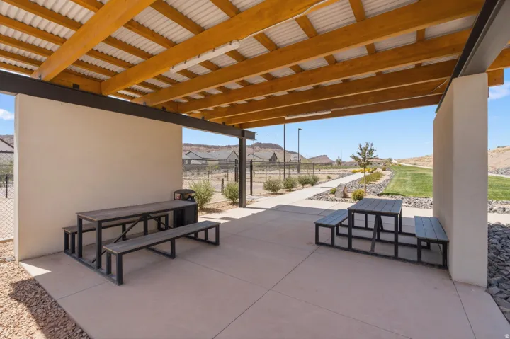 Covered outdoor patio with exposed wood beams, corrugated metal roofing, concrete flooring, and surrounding xeriscape landscaping