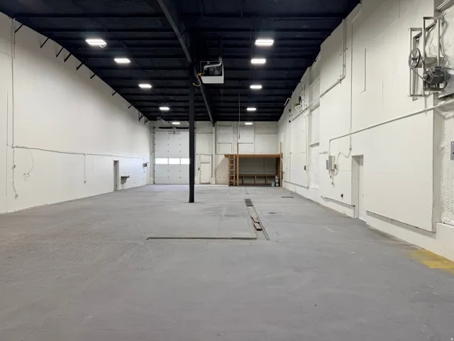 Spacious industrial interior with floor drain and concrete flooring and white walls