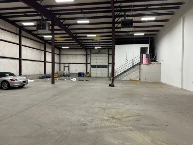 Expansive warehouse space featuring a 16' roll-up door, exposed structural beams, high ceilings, polished concrete flooring, and a mezzanine breakroom with metal railings