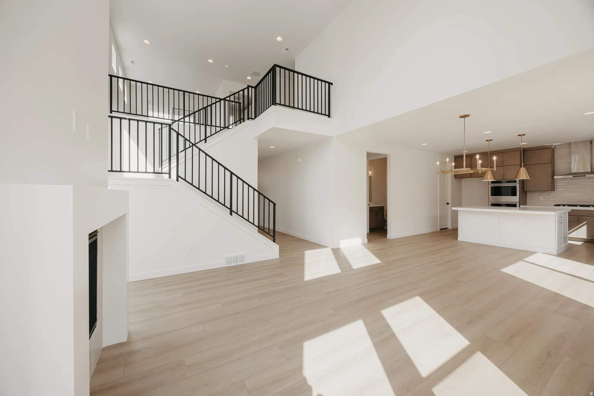 High ceilings, modern staircase with black railings, built-in fireplace, wood-finish flooring, and a kitchen island with pendant lighting