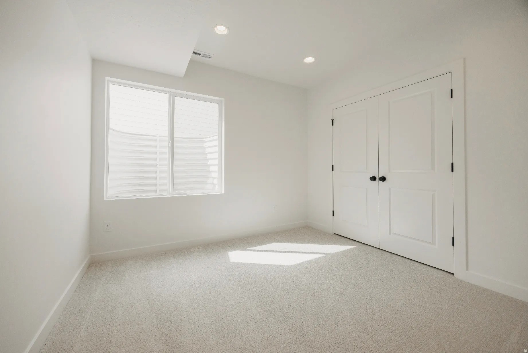 Recessed lighting, light-colored carpeting, white walls, and a window with blinds and a window well