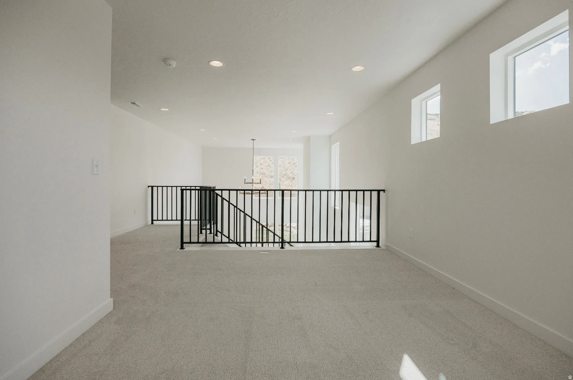 Carpeted loft area with black metal railings, white walls, and recessed lighting