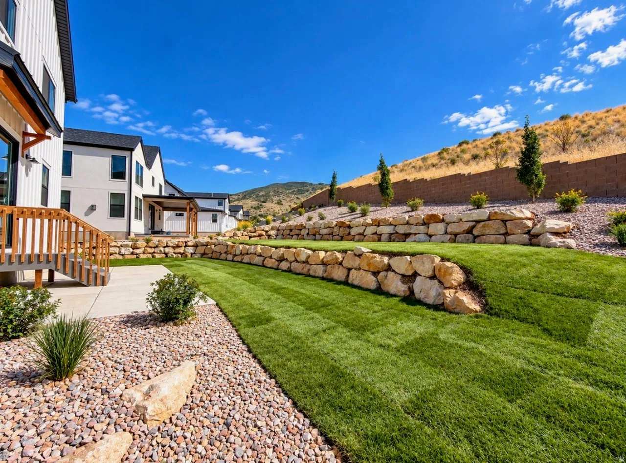Terraced backyard with manicured lawn, natural stone retaining walls, and a concrete patio