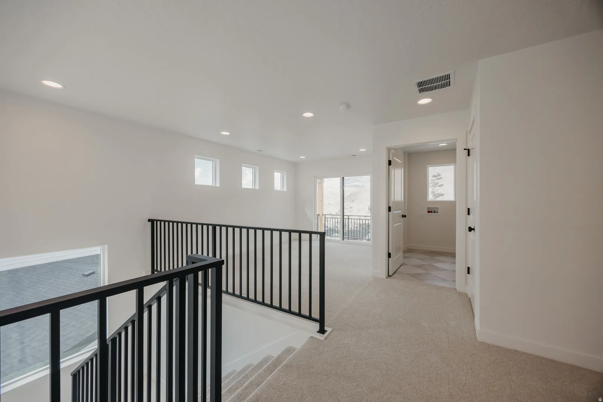 Open upper level with recessed lighting, carpet flooring, a modern black metal railing, and a balcony with exterior mountain scenery