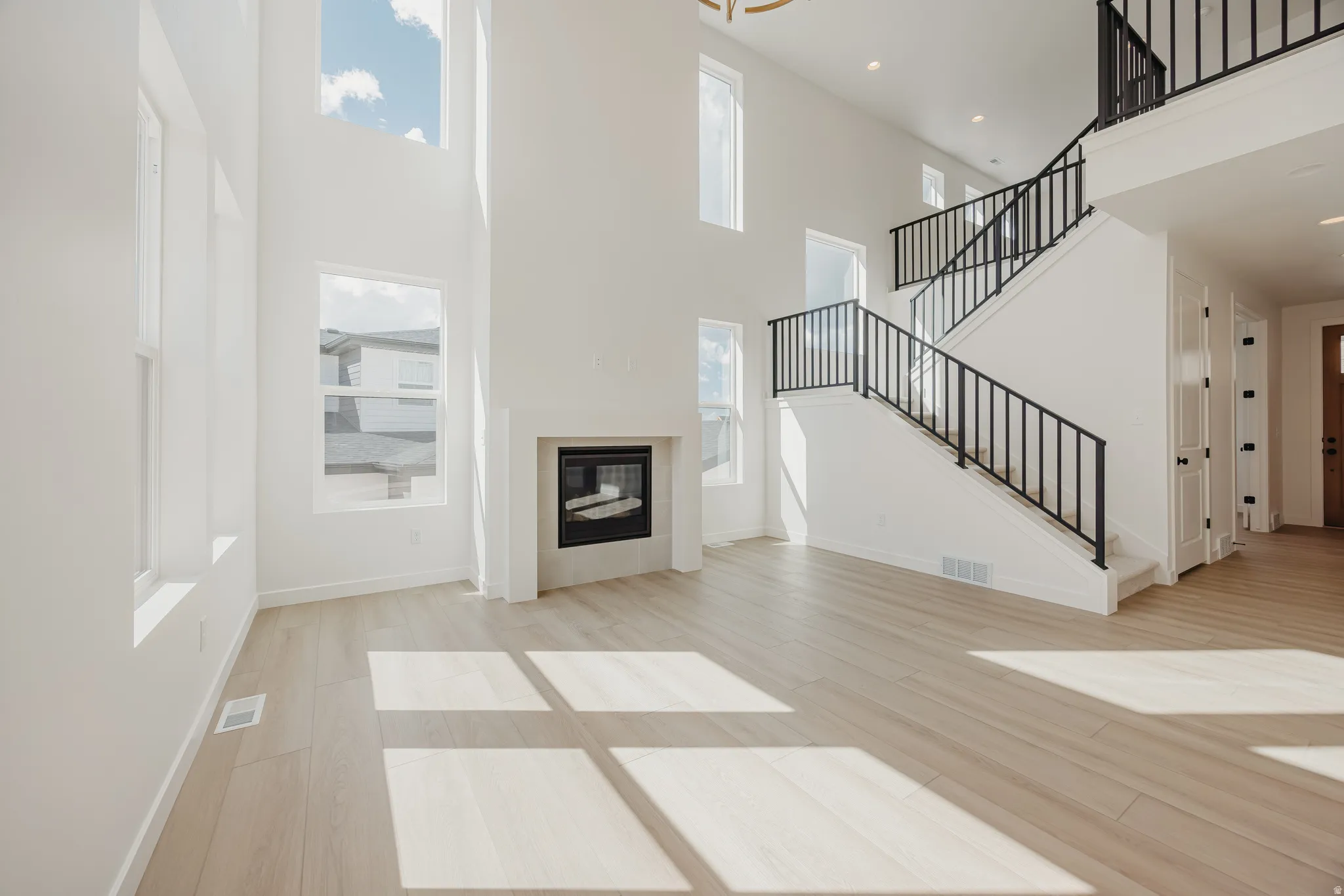 Two-story interior featuring a gas fireplace, light wood-finish flooring, multiple windows, and a staircase with black metal balusters