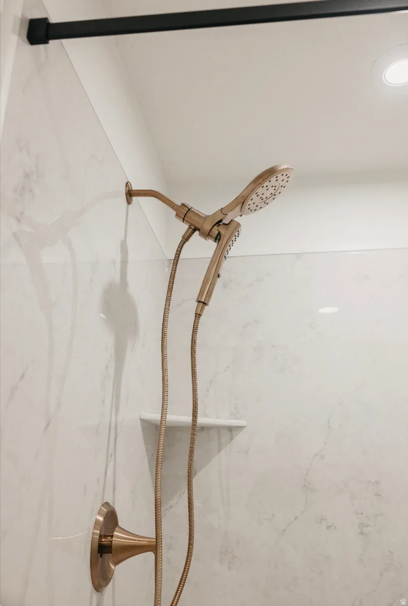 Shower featuring marble-look wall tiling, a built-in corner shelf, and a bronze-finish dual showerhead fixture