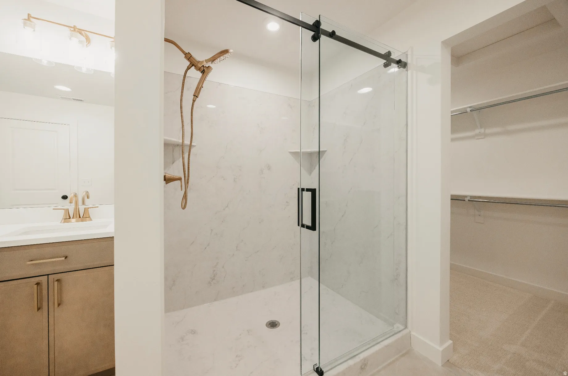 Glass-enclosed shower with a gold-tone shower head, white tiled walls, and a built-in shower niche