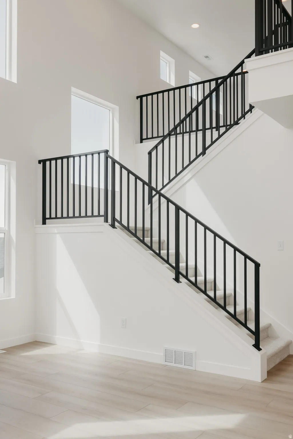 Two-story entryway with high ceilings, contemporary black metal stair railings, light wood-finish flooring, and multiple large windows