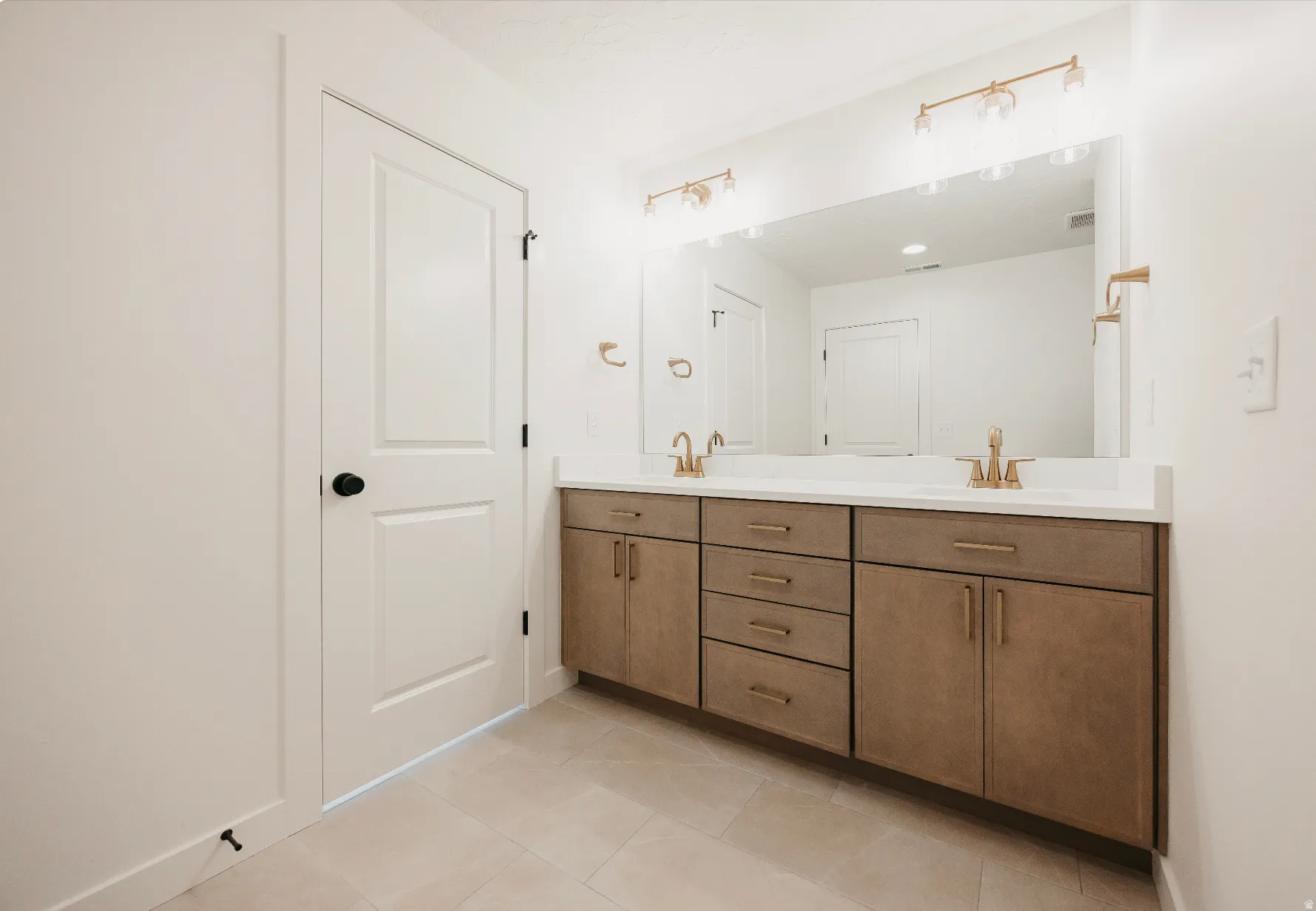 Dual vanity with wood-finish cabinetry, white countertop, and gold-tone fixtures