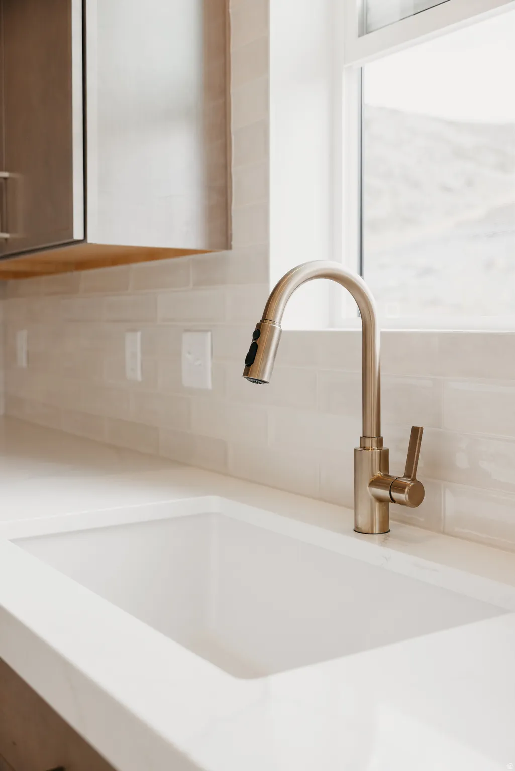 Integrated white sink with a brushed gold-tone faucet, complemented by a subway tile backsplash and light-toned countertop