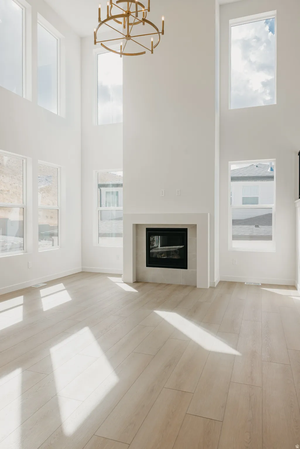 Two-story living area with high ceilings, multiple windows, a modern fireplace, and light wood-finish flooring