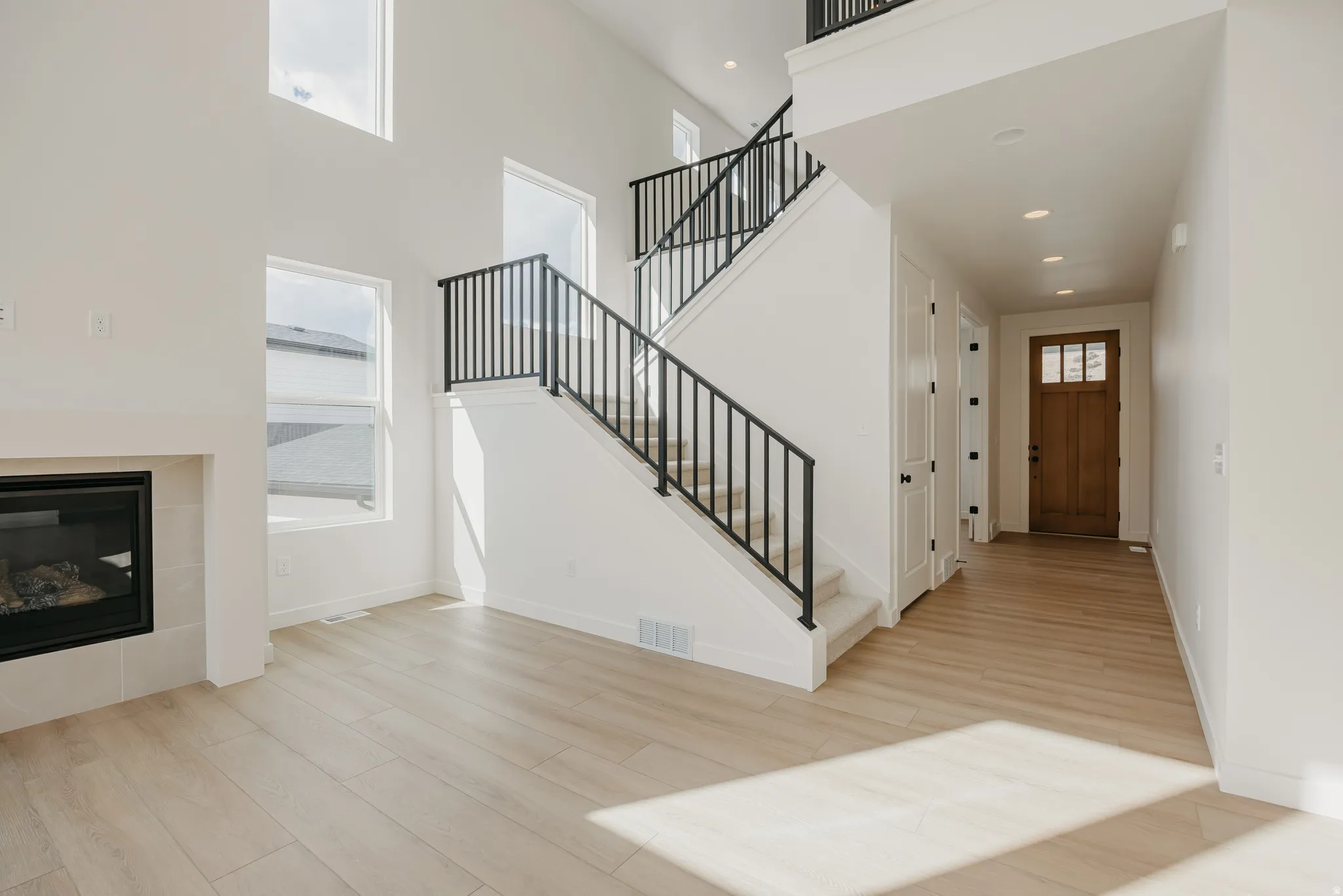 Two-story entry featuring wood-finish flooring, a contemporary staircase with black metal balusters, and a fireplace with a light-toned surround