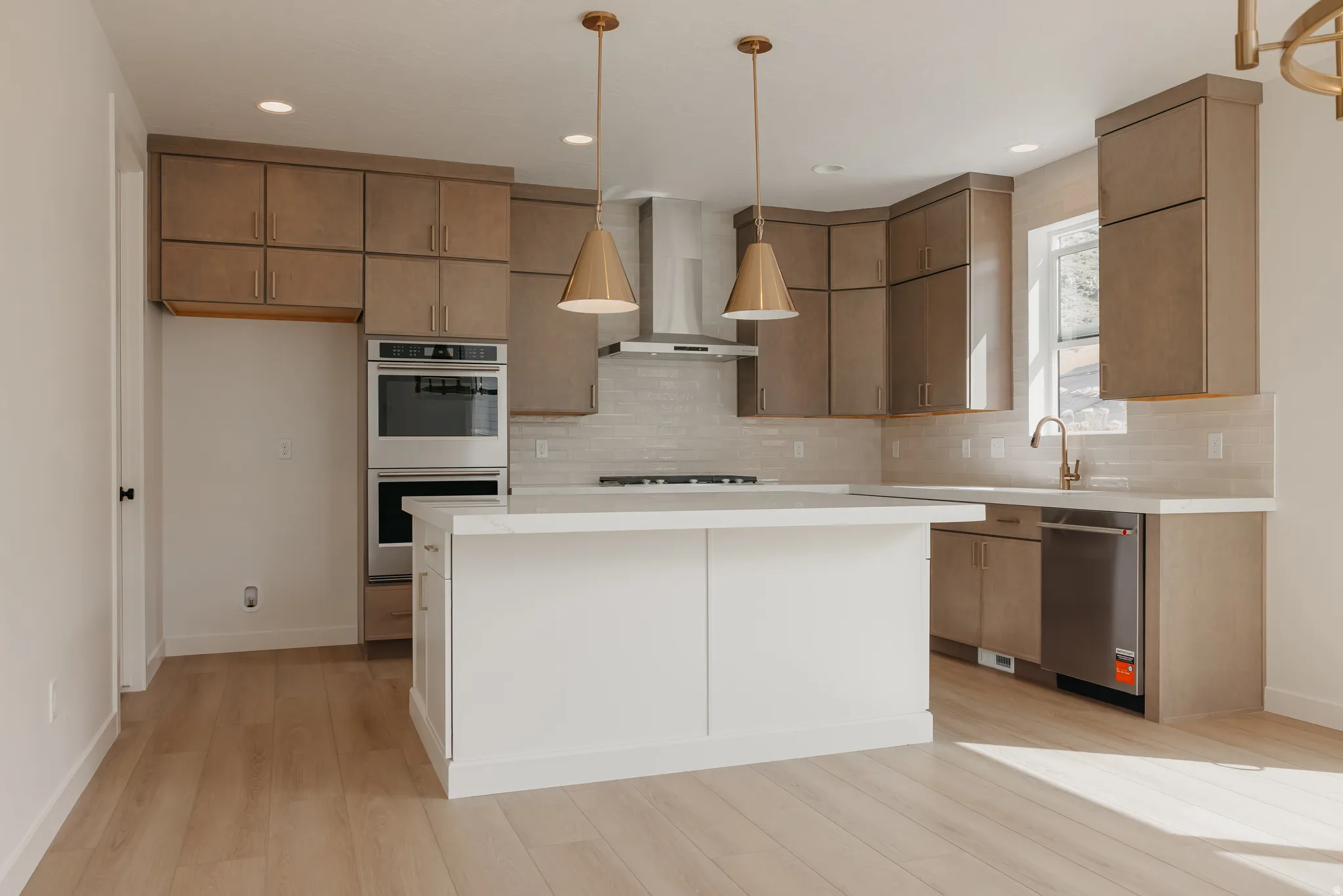 Kitchen featuring wood-finish flooring, a white island, built-in stainless steel double ovens, and warm-toned cabinetry