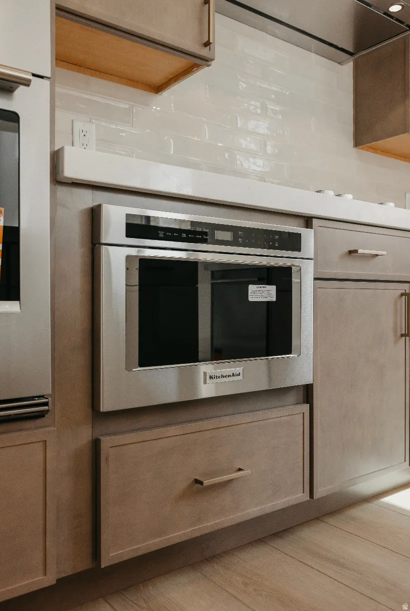 Built-in stainless steel microwave, light wood-finish flooring, light-toned cabinetry with brass hardware, and a white subway tile backsplash