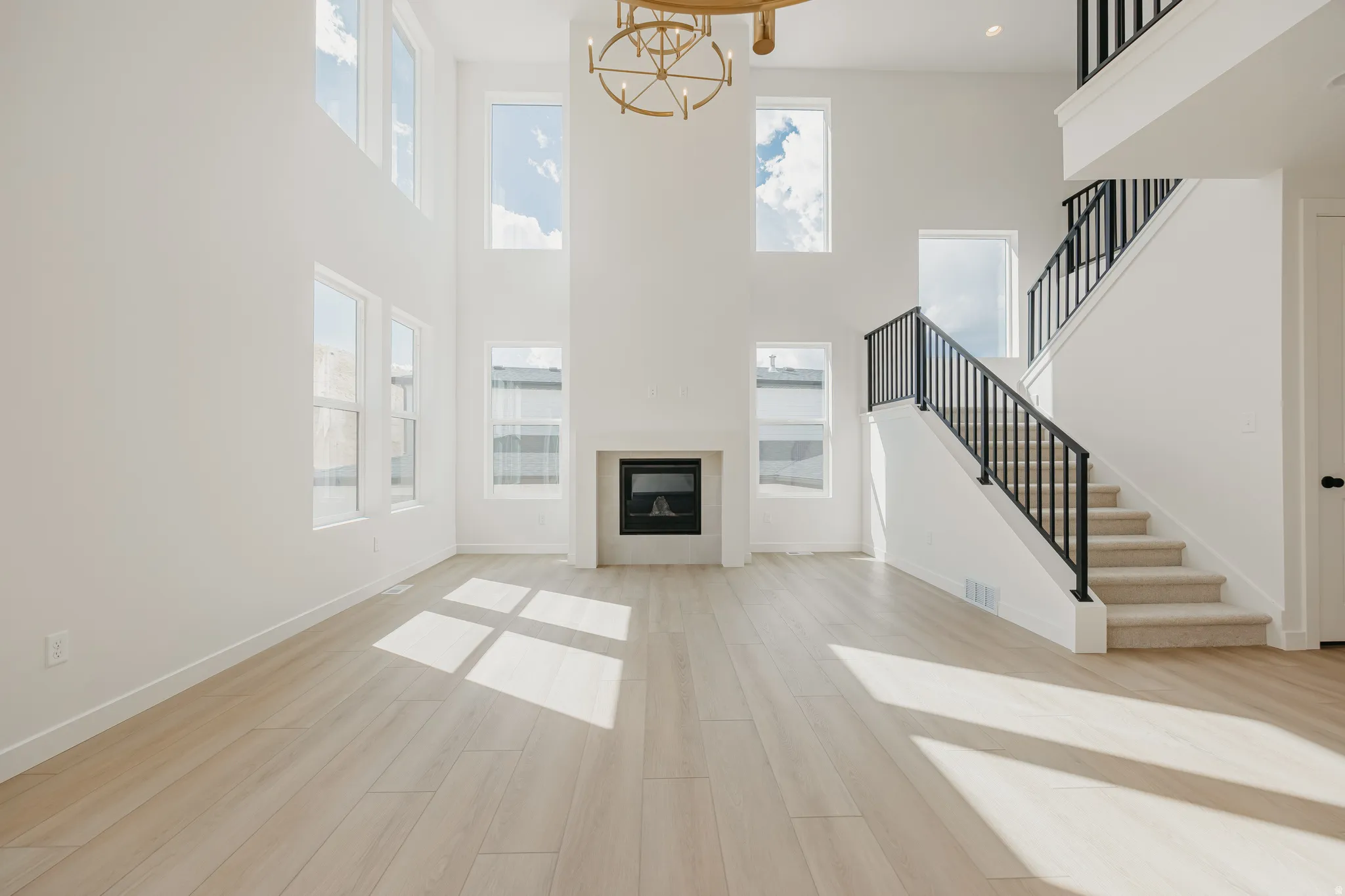 Vaulted ceilings, wood-finish flooring, a contemporary fireplace, and a staircase with black iron railings, complemented by multiple windows
