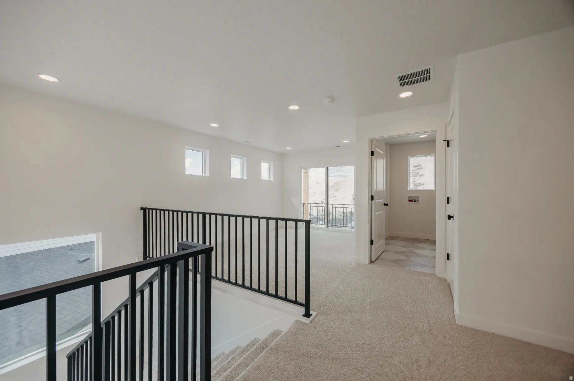 Open loft area with carpeted flooring, recessed lighting, and black metal railings