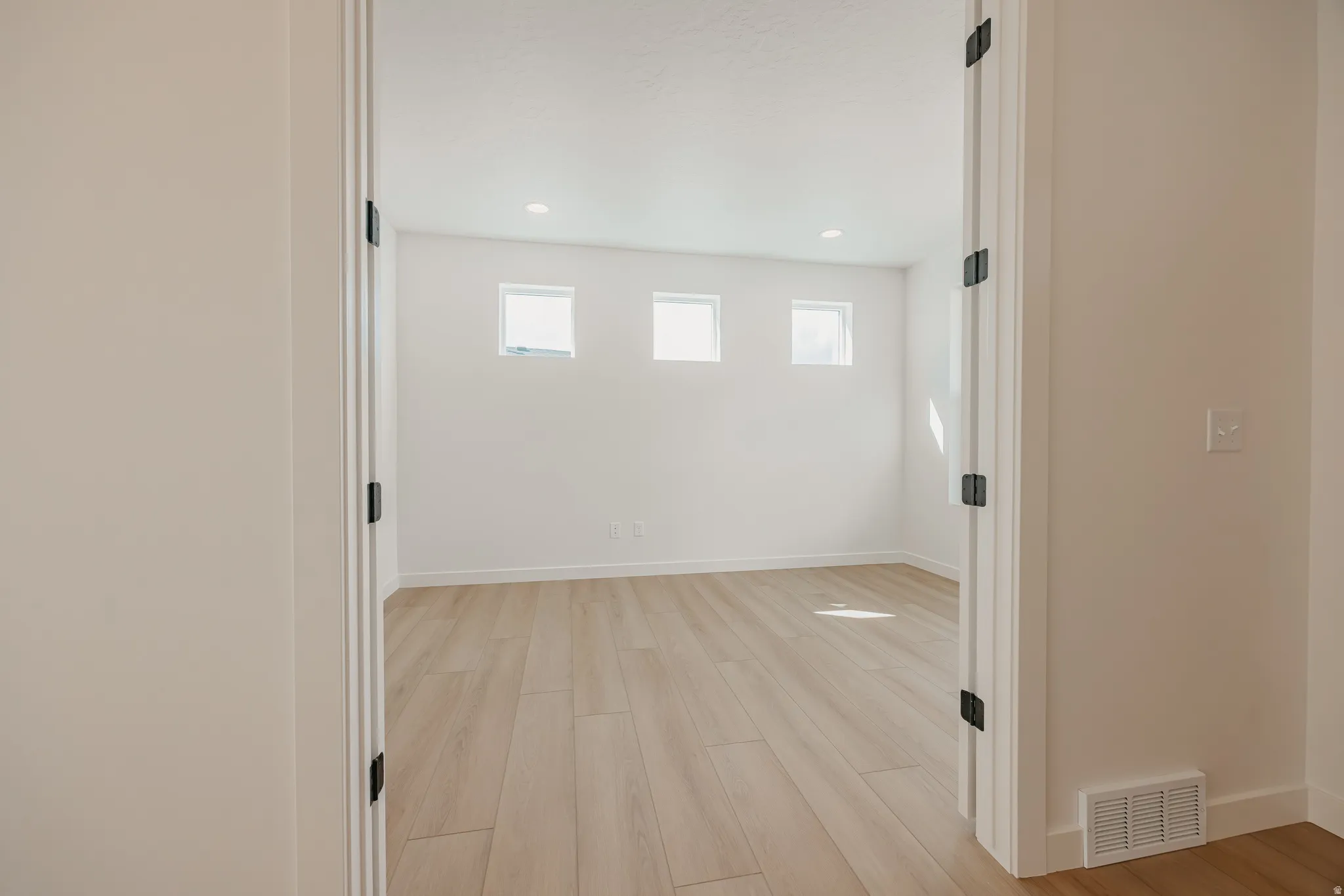 Recessed lighting, wood-finish flooring, white walls, multiple windows, and matte black door hardware