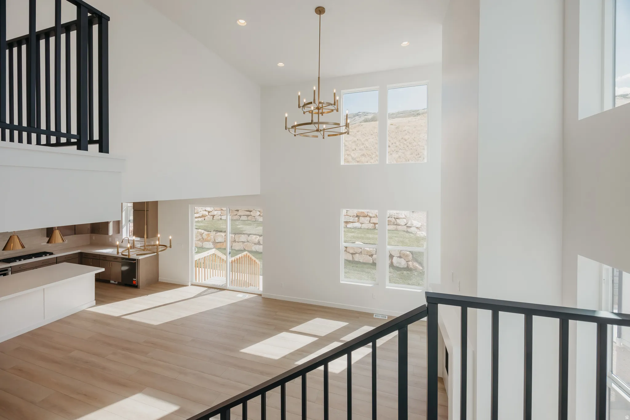 Two-story ceiling, multiple large windows, wood-finish flooring, contemporary chandelier, and a kitchen featuring an island and built-in cabinetry