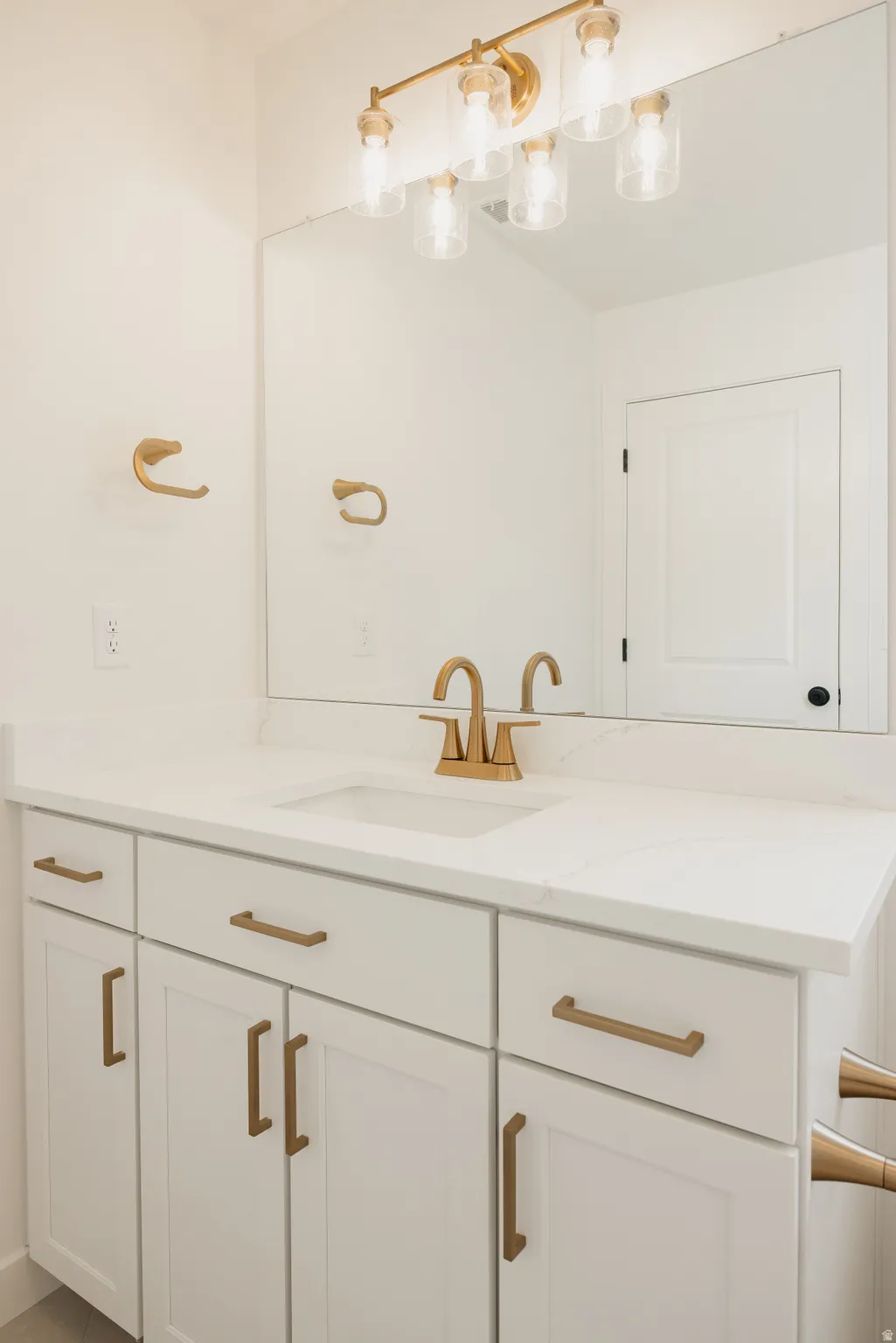White vanity with shaker-style cabinetry, white countertop, undermount sink, and brass-finish hardware