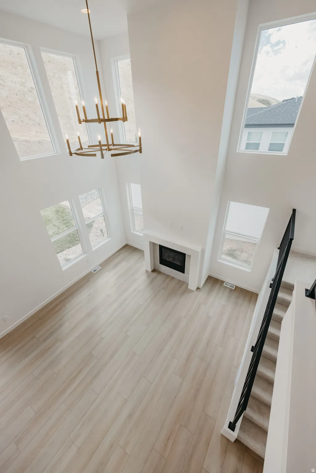 Soaring ceilings with a multi-tiered chandelier, a built-in fireplace, wood-finish flooring, and expansive windows