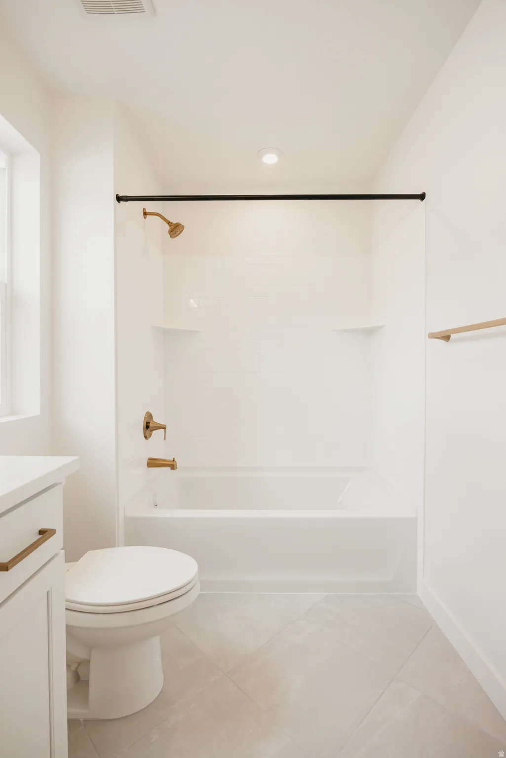 White ceramic bathtub with bronze-finish fixtures, white tile surround, and light-toned tile flooring