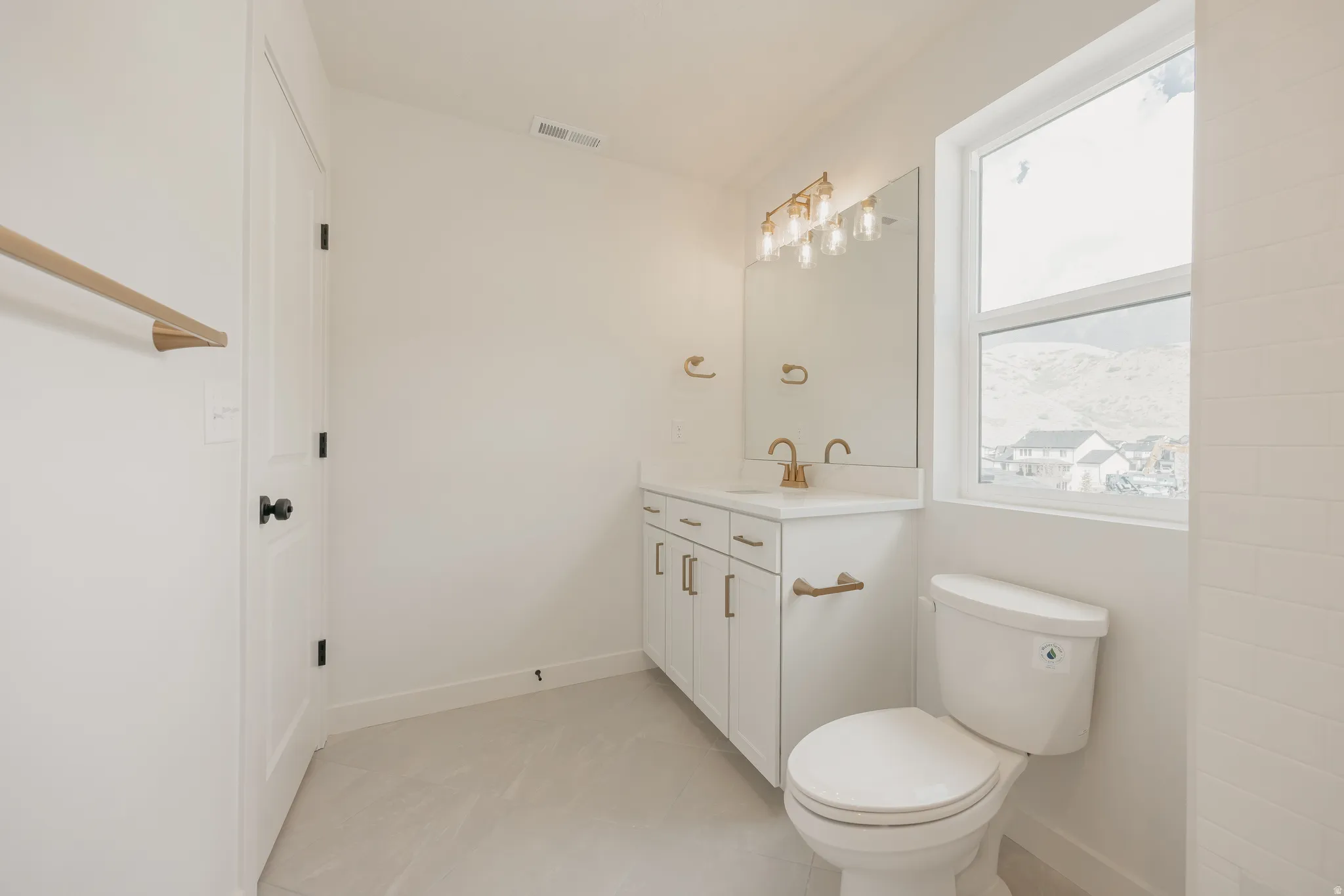 White shaker vanity with gold-finish hardware, rectangular mirror, and wall-mounted light fixture