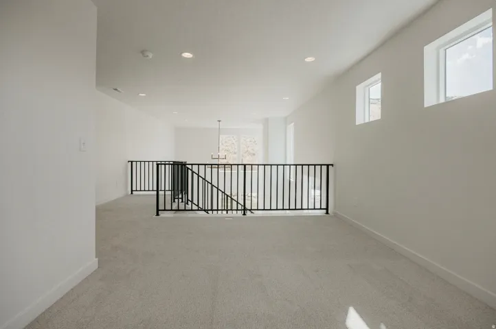 Carpeted loft area with black metal railings, white walls, and recessed lighting