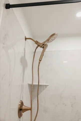 Shower featuring marble-look wall tiling, a built-in corner shelf, and a bronze-finish dual showerhead fixture