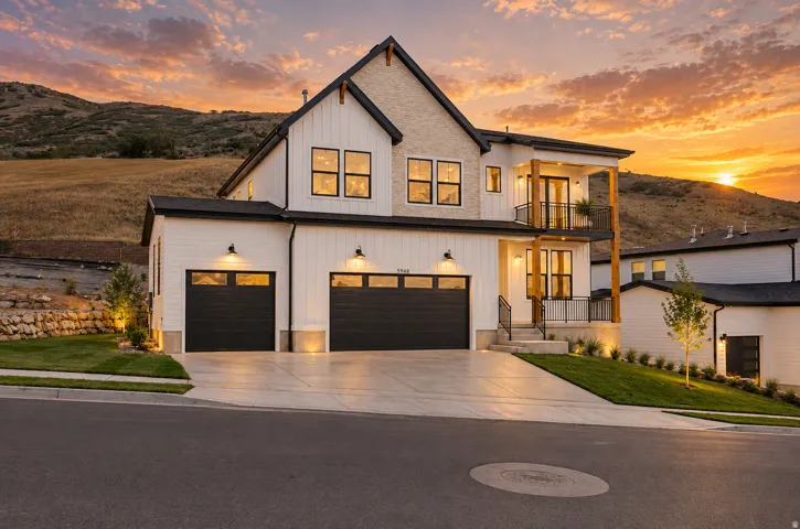 Modern farmhouse exterior with white board-and-batten siding, black-framed windows, a two-car garage with black doors, and an upper-level balcony featuring a black railing and wood-finish columns. Dusk view created with AI enhancement