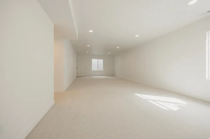 Recessed lighting illuminates a spacious room featuring light-toned carpeting and a window with horizontal blinds