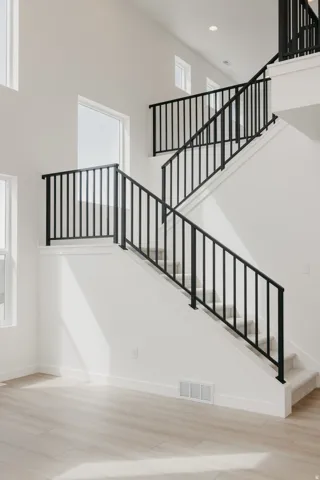 Two-story entryway with high ceilings, contemporary black metal stair railings, light wood-finish flooring, and multiple large windows