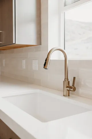 Integrated white sink with a brushed gold-tone faucet, complemented by a subway tile backsplash and light-toned countertop
