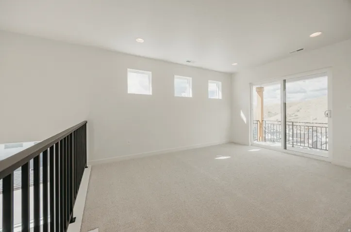 Spacious room featuring light-colored carpeting, recessed lighting, multiple transom windows, and a sliding glass door leading to a balcony with metal railings