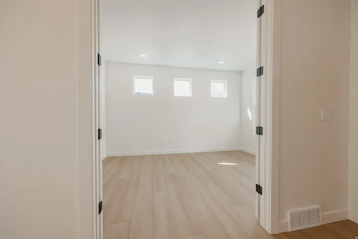 Recessed lighting, wood-finish flooring, white walls, multiple windows, and matte black door hardware