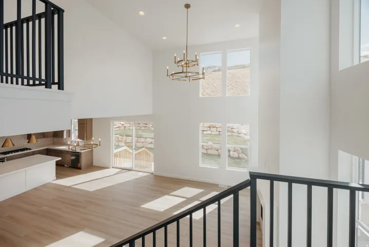 Two-story ceiling, multiple large windows, wood-finish flooring, contemporary chandelier, and a kitchen featuring an island and built-in cabinetry