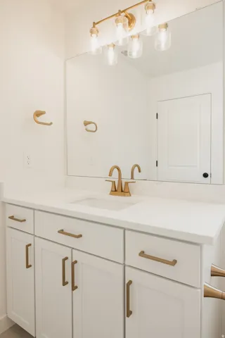 White vanity with shaker-style cabinetry, white countertop, undermount sink, and brass-finish hardware