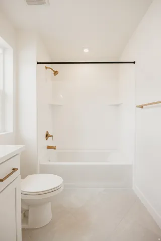 White ceramic bathtub with bronze-finish fixtures, white tile surround, and light-toned tile flooring