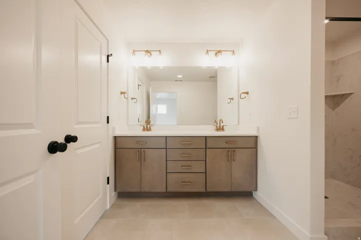 Dual vanity with integrated sinks, brushed gold fixtures, a large mirror, and recessed lighting