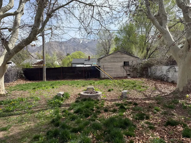 Expansive backyard featuring a stone fire pit, mature trees, and a mountain backdrop