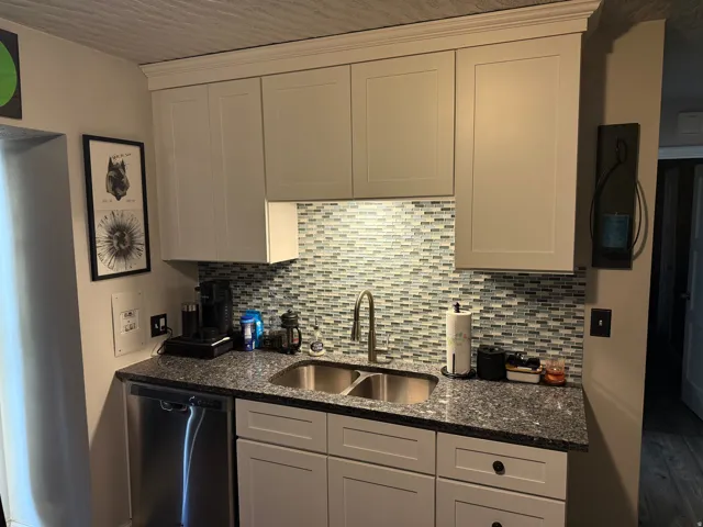 Contemporary kitchen featuring light-toned cabinetry, granite-style countertops, a mosaic tile backsplash, a stainless steel double-basin sink, and a stainless steel dishwasher