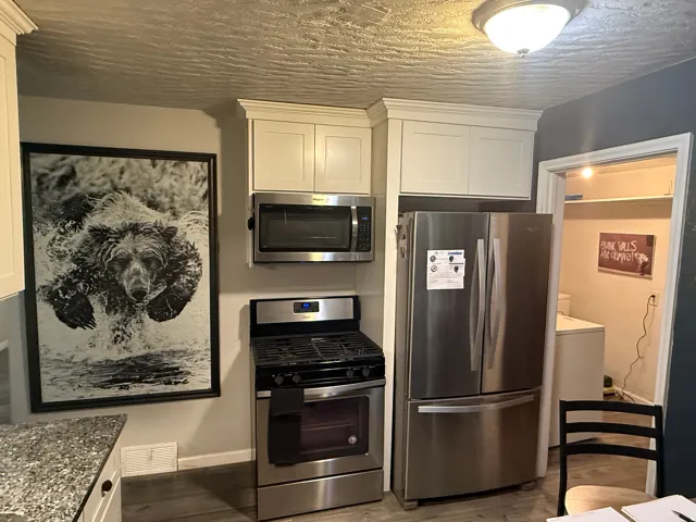 Stainless steel gas range, stainless steel microwave, stainless steel refrigerator, white shaker-style cabinetry, and granite-finish countertops