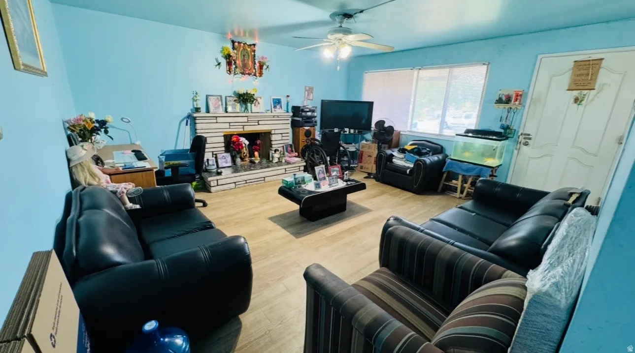Wood-finish flooring, a stone-faced fireplace with hearth, a ceiling fan, and large windows
