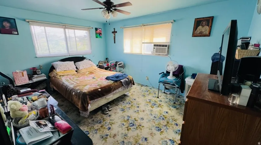 Room featuring a ceiling fan, two windows with roller shades, and a wall-mounted air conditioning unit