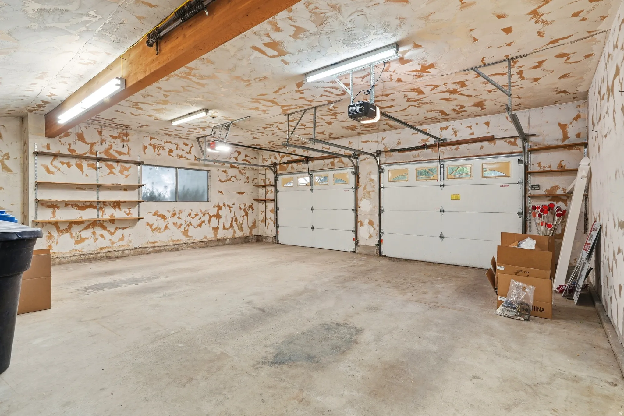 Concrete flooring, two automatic garage door openers, two overhead fluorescent light fixtures, two garage doors with window panels, and built-in shelving
