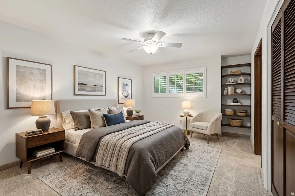 White walls with light-colored carpeting, a white ceiling fan, a window with plantation shutters, and a built-in shelving unit