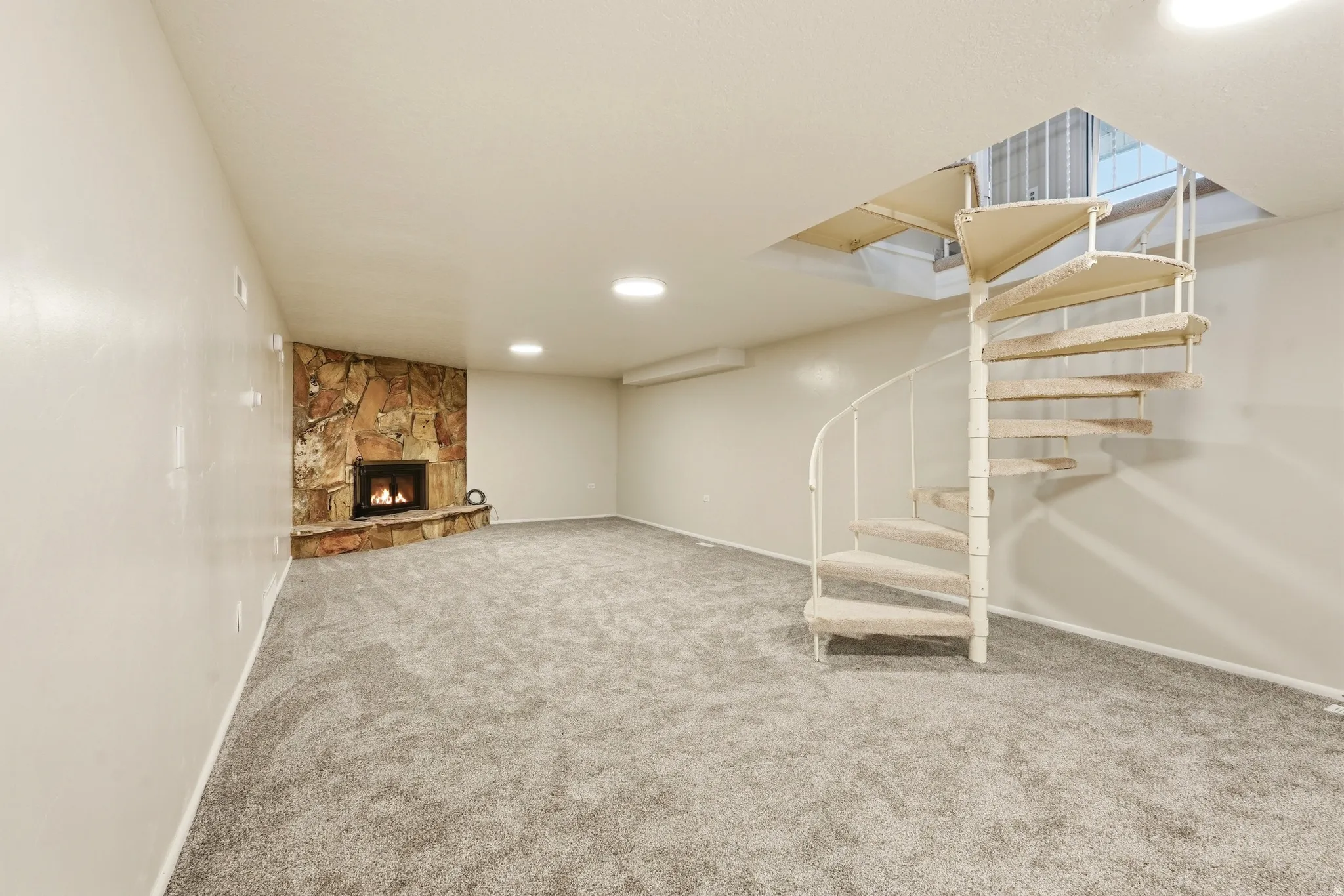 Spiral staircase, recessed lighting, corner stone-clad fireplace, and neutral carpeting