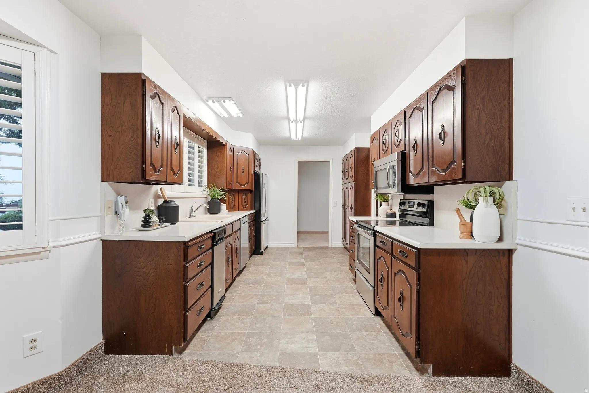 Galley kitchen with wood-finish cabinetry, white countertops, and stainless steel appliances