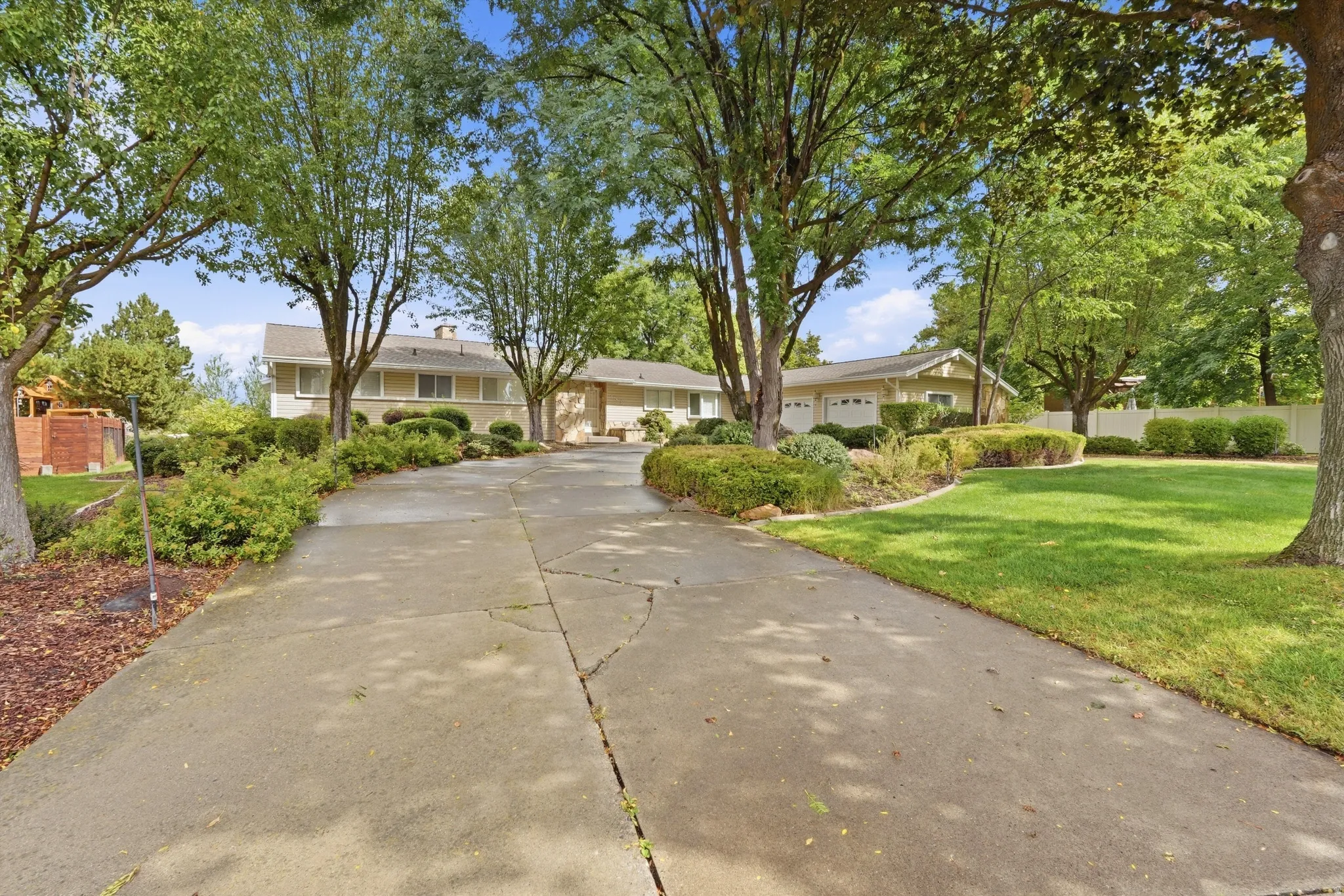 Expansive driveway with a landscaped island, mature trees, and a manicured lawn