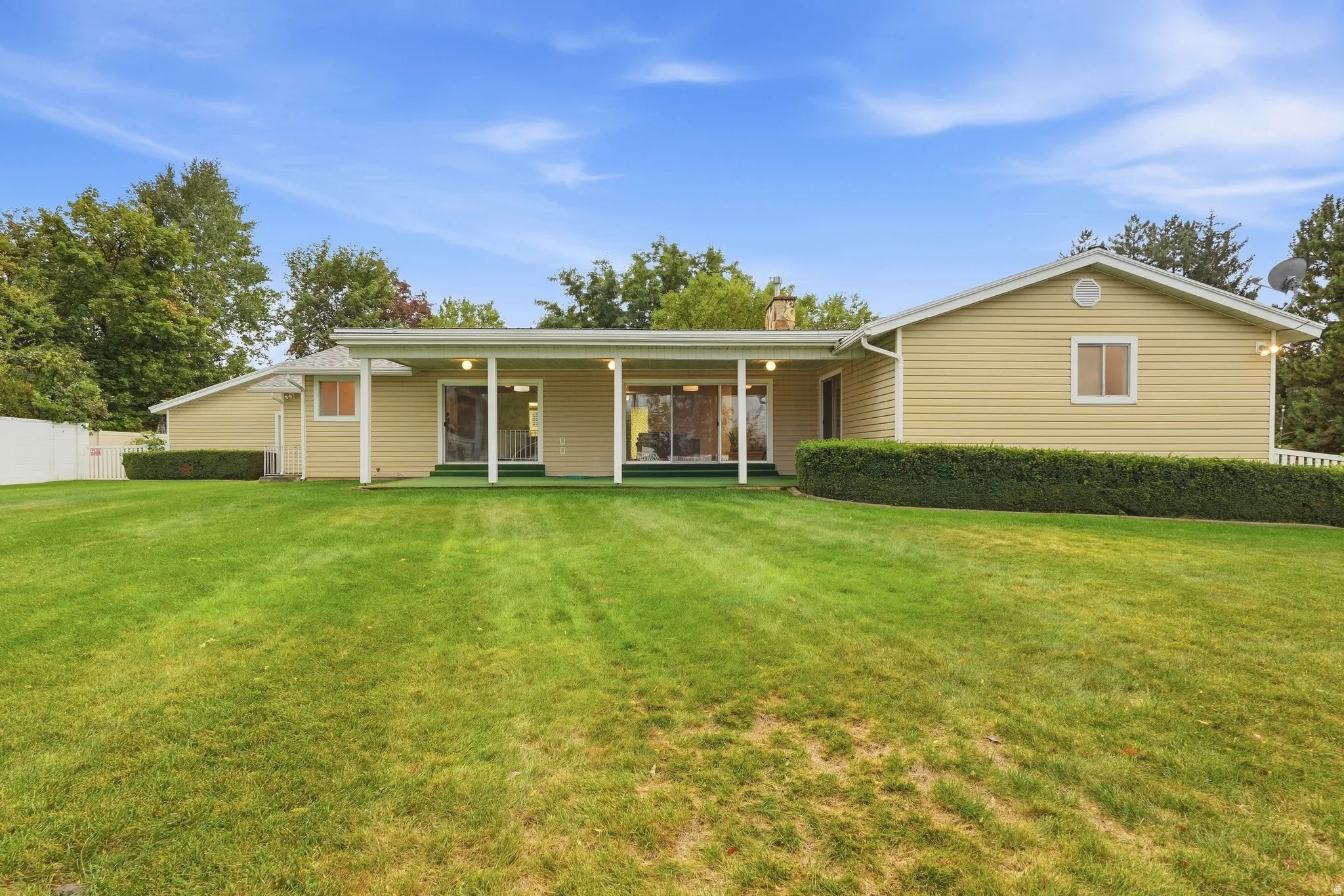 Spacious lawn area with a covered patio featuring multiple sliding glass doors and white columns