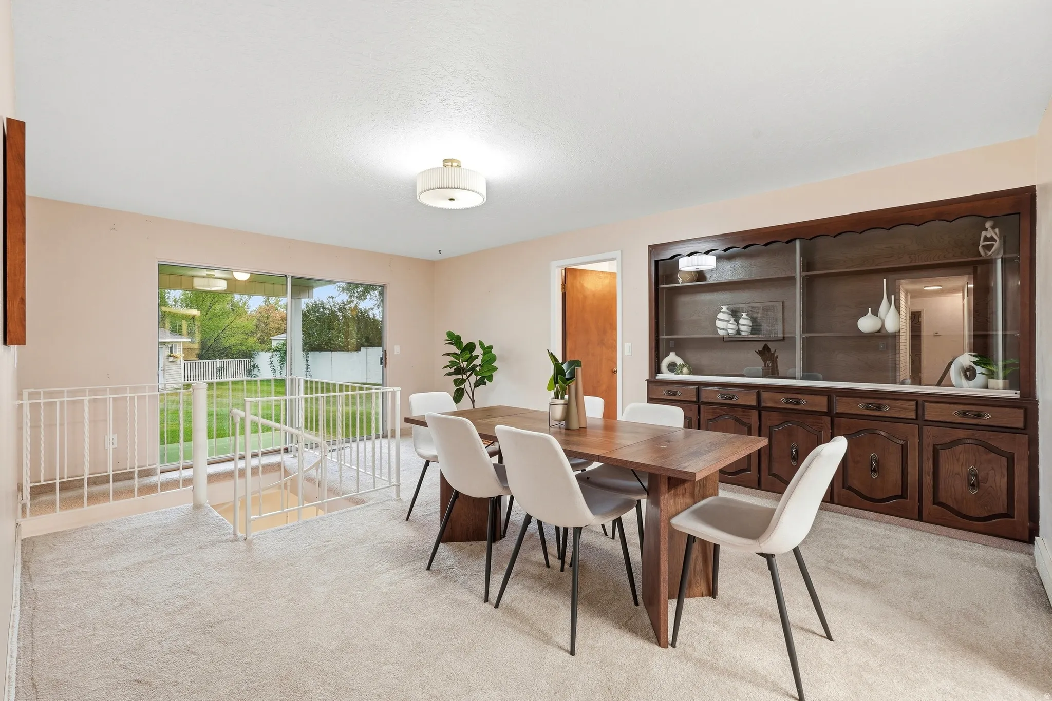 Elegant dining room featuring a wood-finish dining table, upholstered chairs, and abundant natural light from dual glass doors opening to a private outdoor space